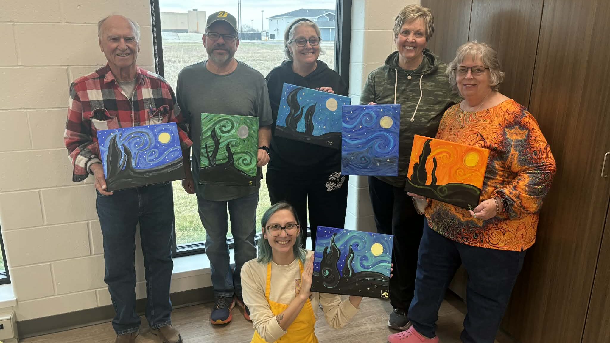Group photo of people posing with paintings they created in group instruction