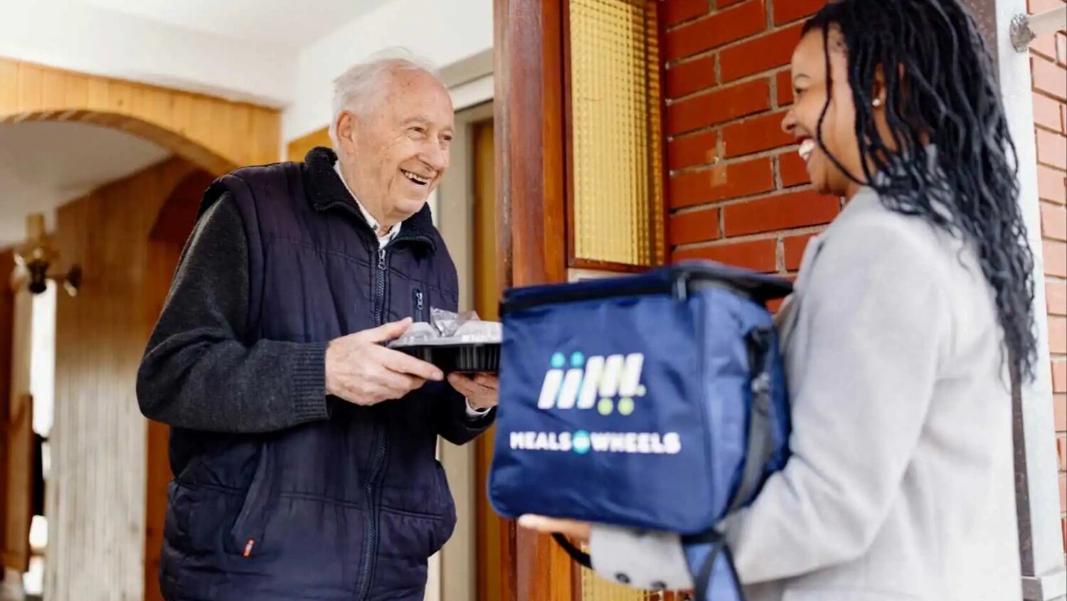 Man receiving meals on wheels delivery from woman